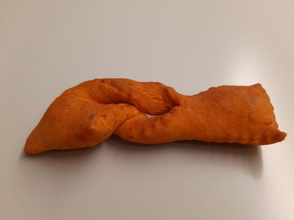 Das Foto zeigt ein Teiggebäck. Es ist länglich und rechteckig. In der Mitte hat es einen Schlitz und die Seiten sind leicht verdreht.