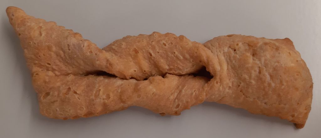 Das Foto zeigt ein braunes Teiggebäck. Es ist länglich, fast rechteckig, mit einem Schlitz in der Mitte und etwas verdrehten Seitenteilen.
