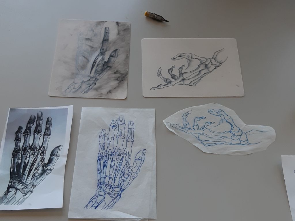 Auf einem grauen Tisch liegen fünf Blätter mit Zeichnungen von Händen. Es sind eher Skeletthände, denn normale Hände.
