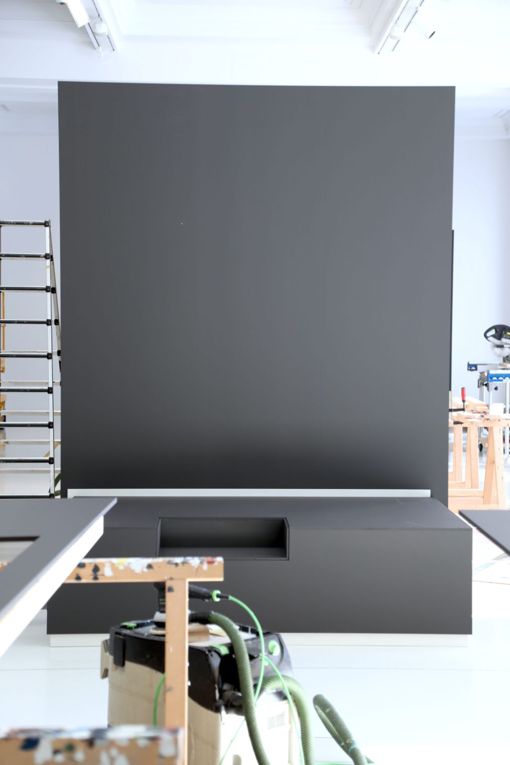 Ein grosser, schwarzer Hintergrund steht in einem hellen Raum, von Leitern und Werkzeugen umgeben