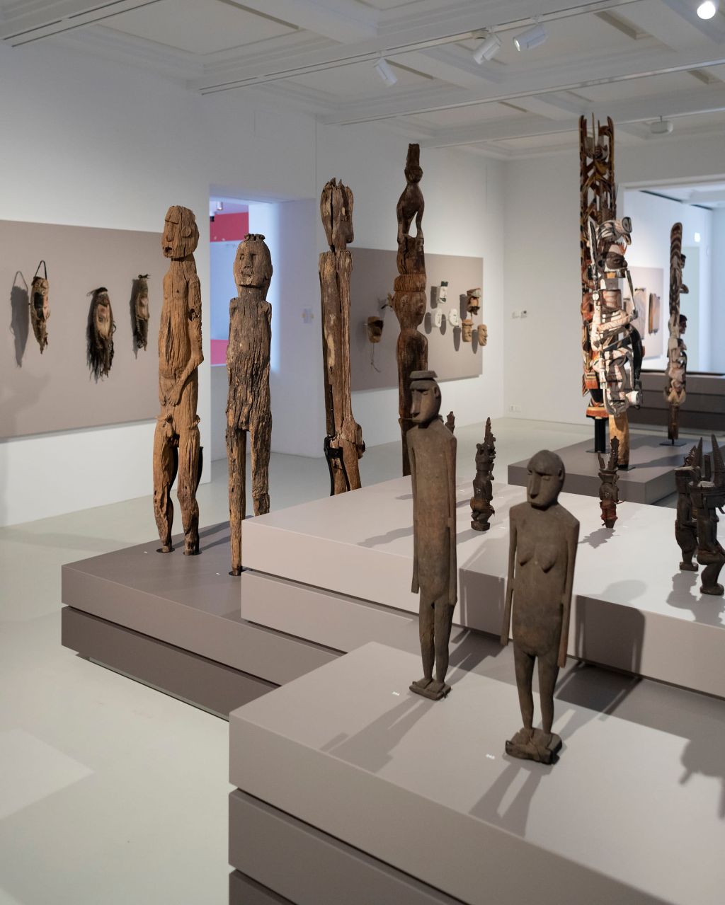 Holzskulpturen in verschiedenen Grössen stehen in einem hellen Ausstellungsraum auf Podesten in verschiedenen Braun- und Grautönen