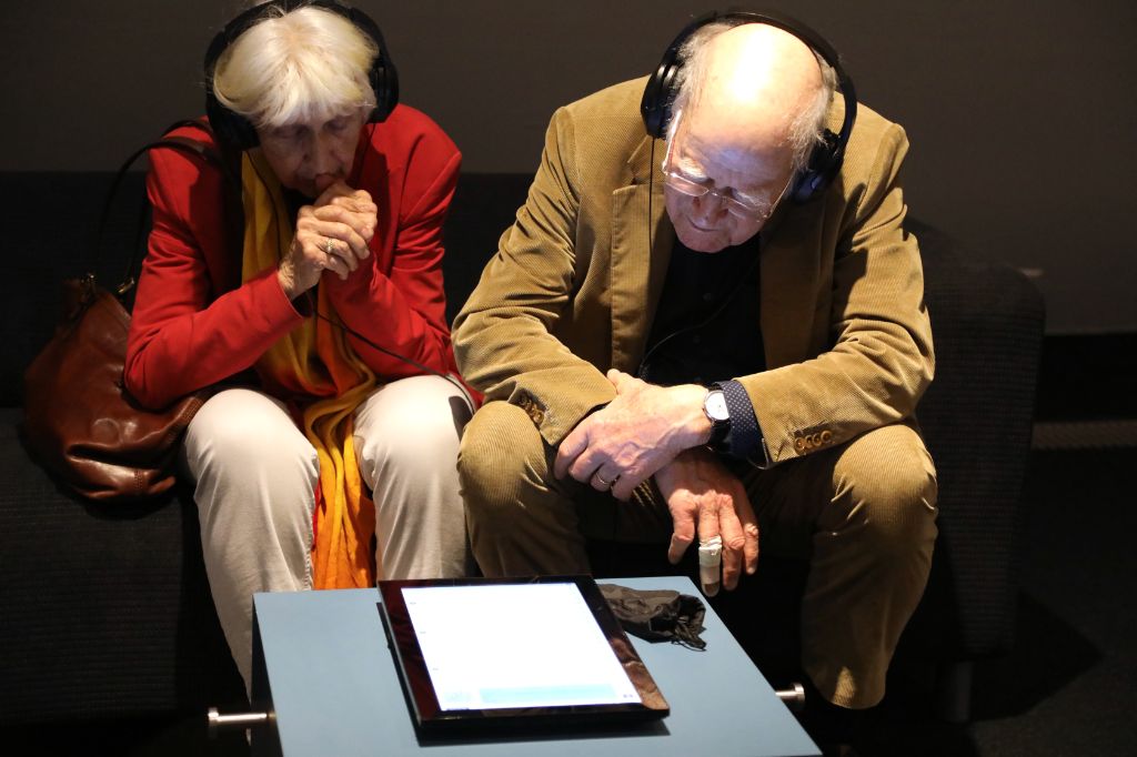 Ein älteres Paar hört mit Kopfhörern interessiert einem Audioguide auf einem Tablet zu