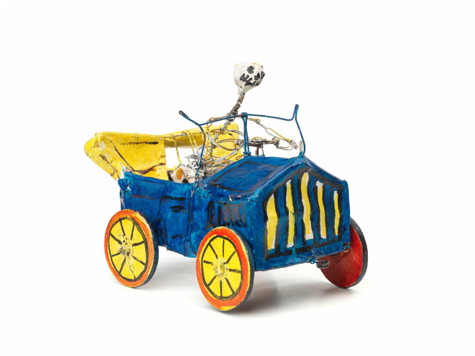 Mexikanische Totenfigur aus Pappmache, in Form eines Skeletts, welches ein blaues Oldtimer-Auto mit offenem gelben Verdeck, roten Rädern mit gelben Felgen steuert.