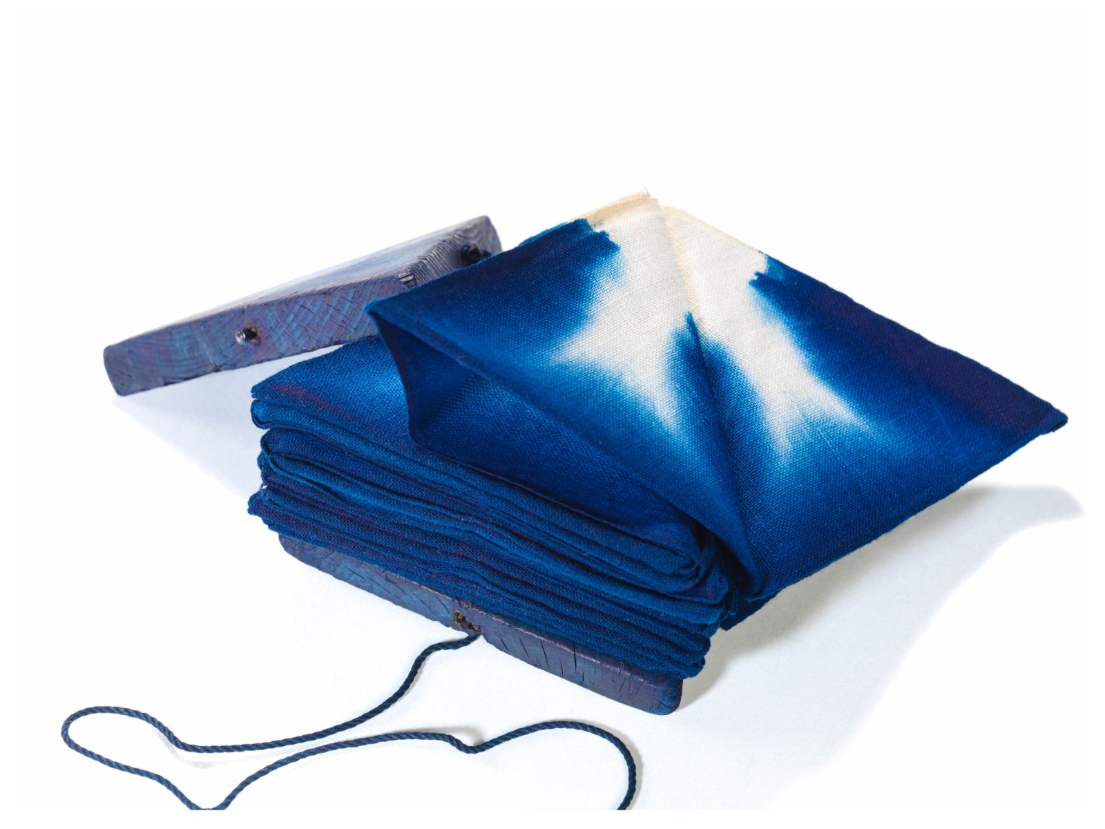 The folded indigo-dyed fabric is pressed with triangular wooden boards.