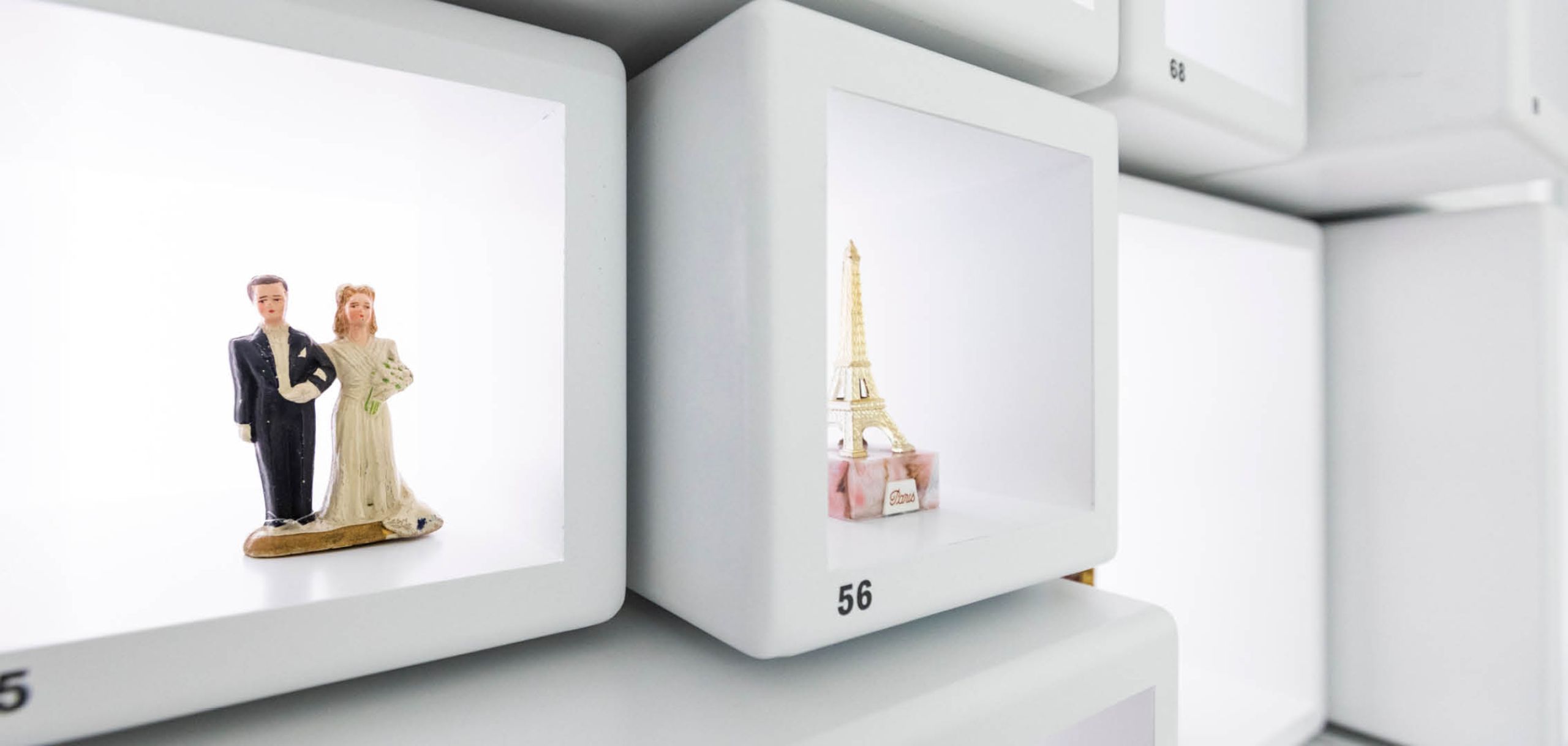 Ausschnitt aus einem weissen Setzkasten. Im Kästchen links steht ein Miniatur-Brautpaar. Im Kästchen rechts ein Miniatur-Eiffelturm.